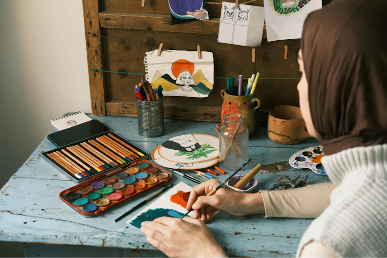 A woman in a hijab paints at a desk