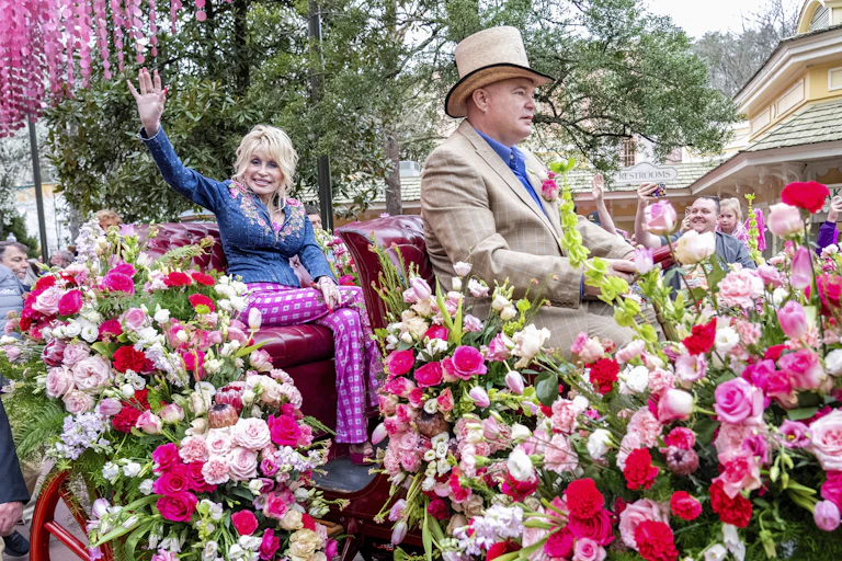 Dolly Parton waves aboard a flower-strewn wagon.