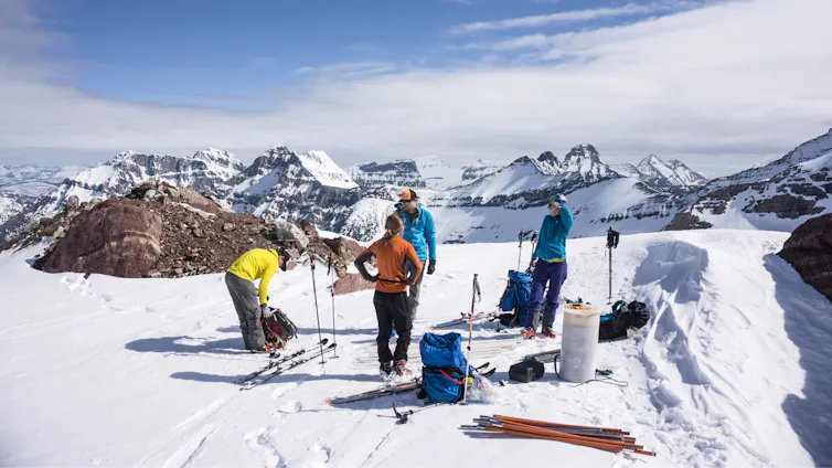 Scientists on skis stand on a glacier with mountains in the background.