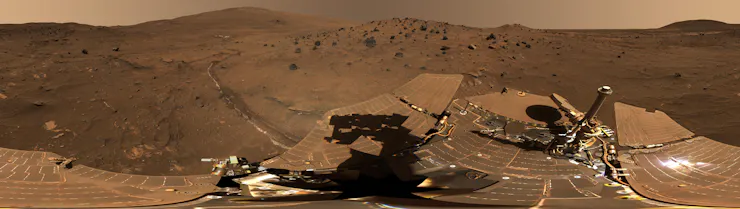 A panoramic view of a rocky, barren landscape with metallic equipment in the foreground.