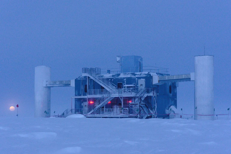 A building with a tower at each end stands in the middle of a barren ice sheet, with the Moon rising behind it.