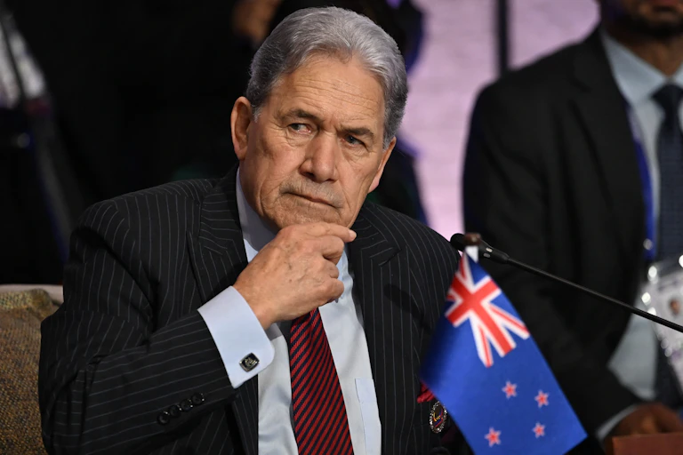 NZ foreign minister Winston Peters stroking chin with NZ flag in foreground
