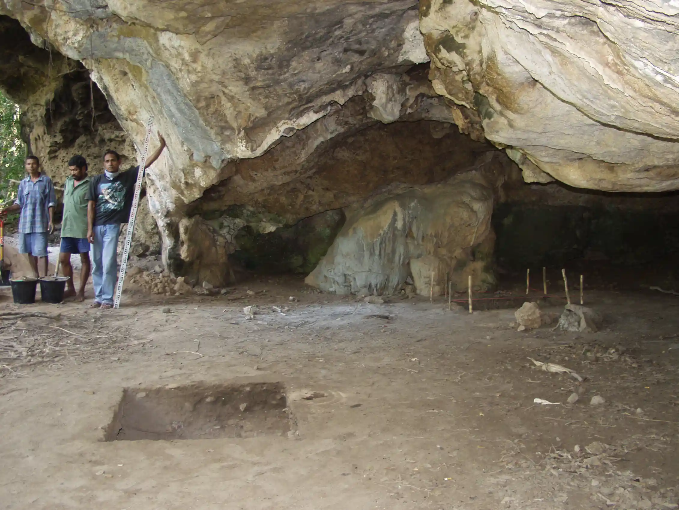 Three people stand at the side of a cave with a dirt floor