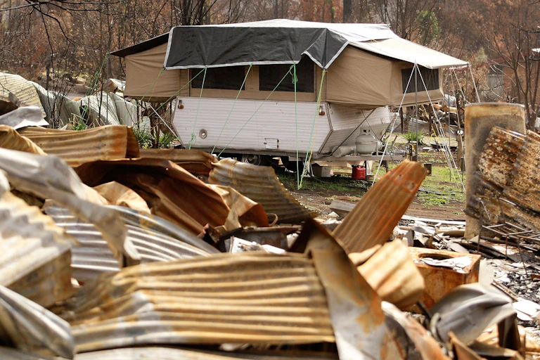 A caravan is parked near the remains of a house destroyed by a bushfire.