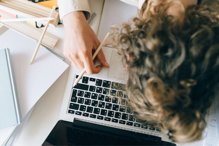 A woman rests her head on top of a laptop and books.