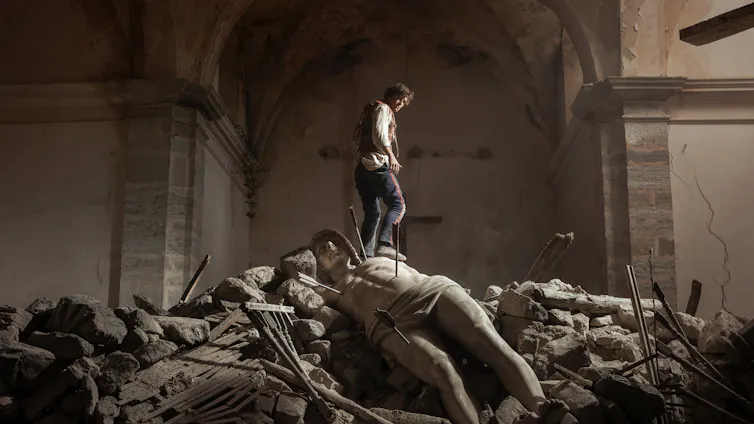 Film still: a man in a museum, standing on a pile of ruined statues.