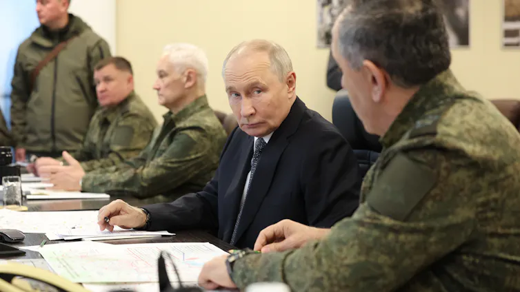 Vladimir Putin sat at a desk alongside Russian military officials.