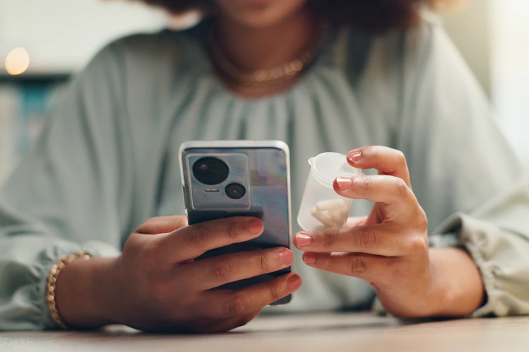 A woman holding a phone in one hand and a bottle of pills in the other.