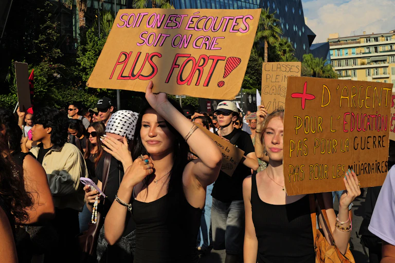 Gros plan sur des manifestantes qui tiennent des pancartes avec les slogans, « Soit on est écoutés, soit on crie plus fort ! » et « Plus d'argent pour léducation, pas pour la guerre, pas pour les milliardaires »\
