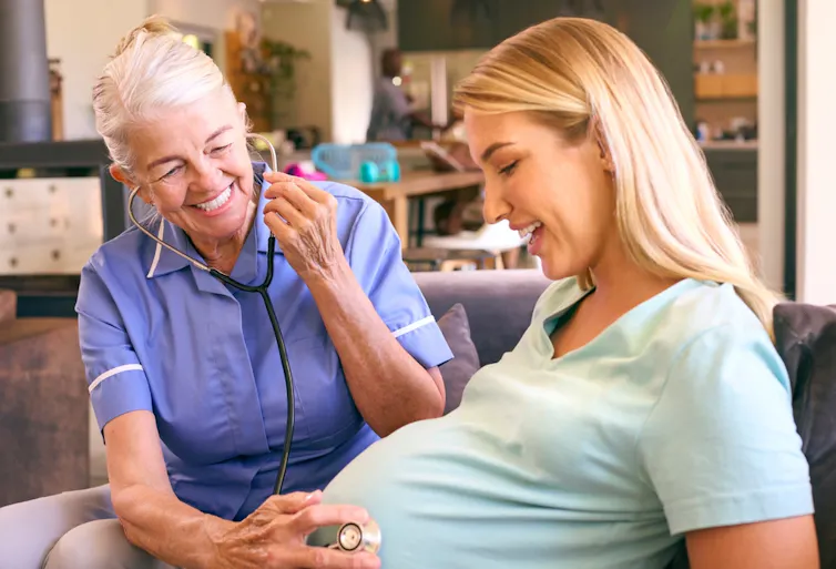 A medic holding a stethoscope to a pregnant woman's belly.