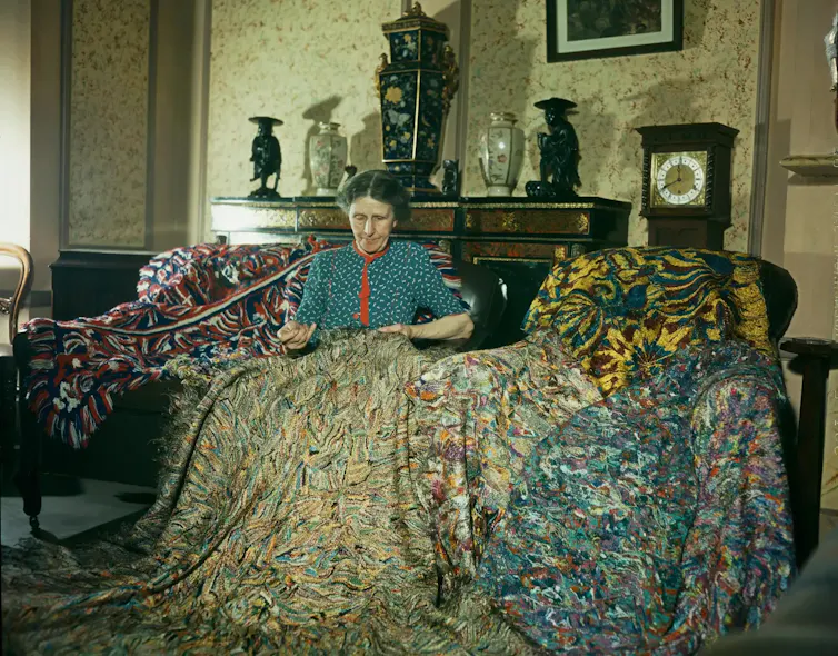 English artist Madge Gill making a rug by inserting left over strands of silk into a canvas backing.