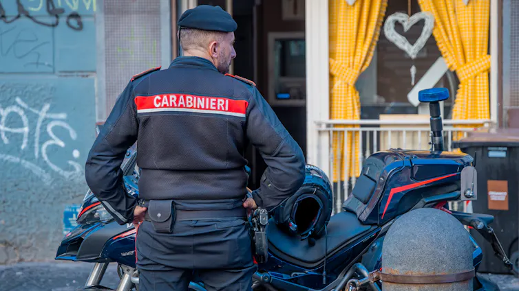 A member of the Carabinieri stands next to his motorbike.