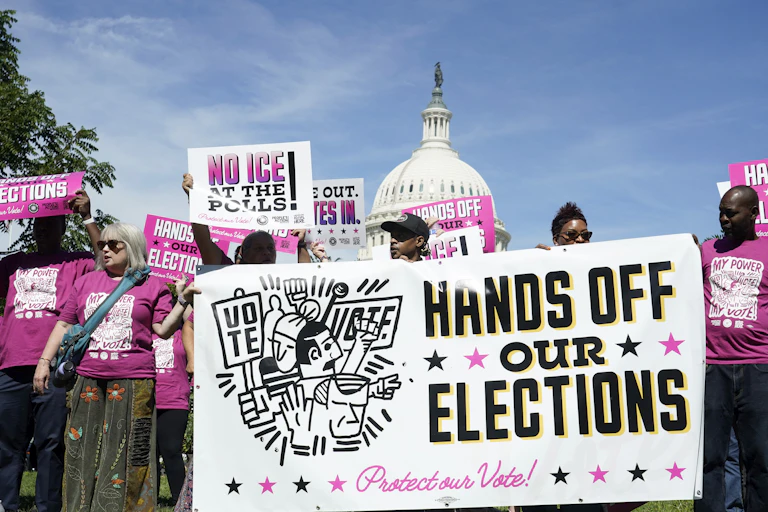 A crowd of people at a rally with some holding a sign that says 'HANDS OFF OUR ELECTIONS.'