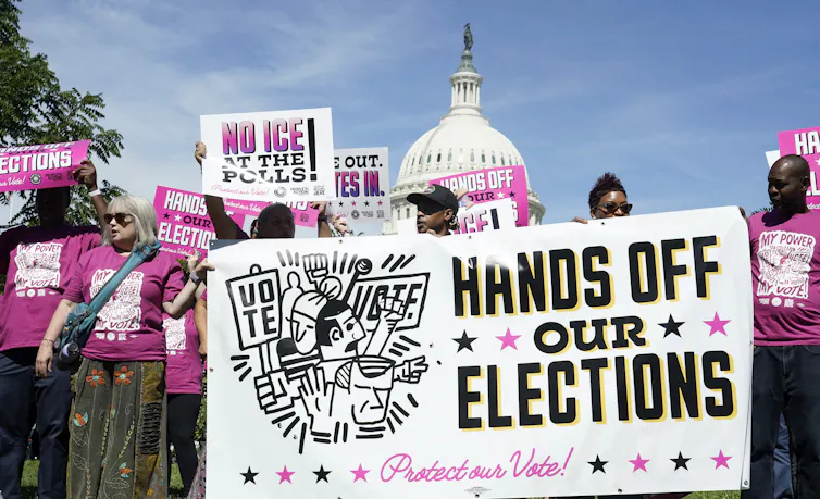 A crowd of people at a rally with some holding a sign that says 'HANDS OFF OUR ELECTIONS.'