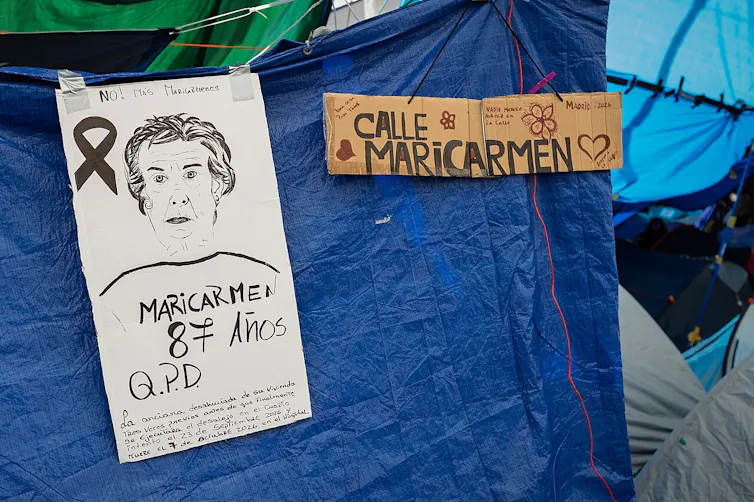 A blue tarpaulin, with a hand-drawn poster and a sign that reads 'Calle Maricarmen'