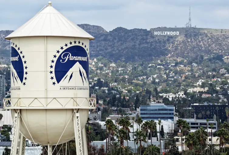 An aerial view of a water tower with houses on a hill in the background.