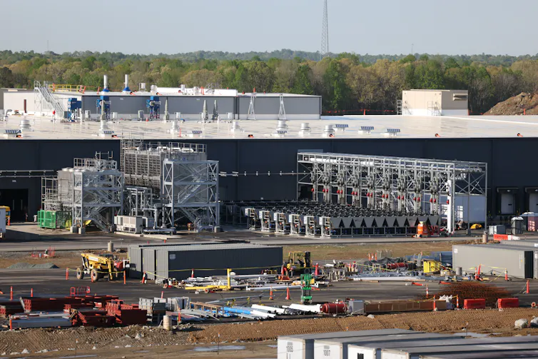 A large building is under construction, with many trucks and other pieces of equipment outside.