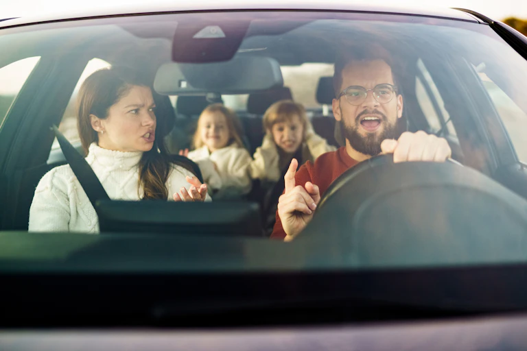 A mother and father arguing in the car while their two children are sitting in the back seats.