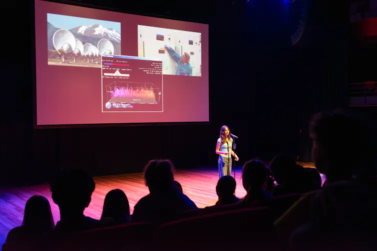 A teenage girl stands on stage giving a presentation.