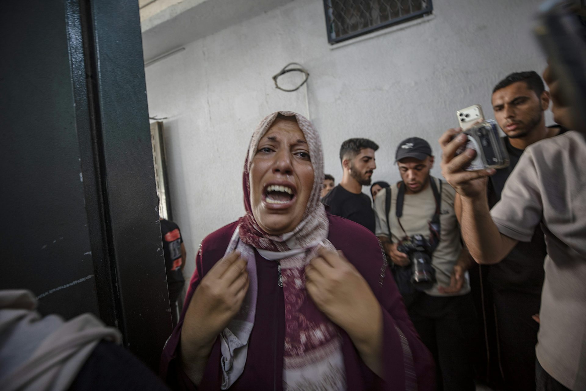 A Palestinian woman cries while people look on. One is filming her on a mobile phone.