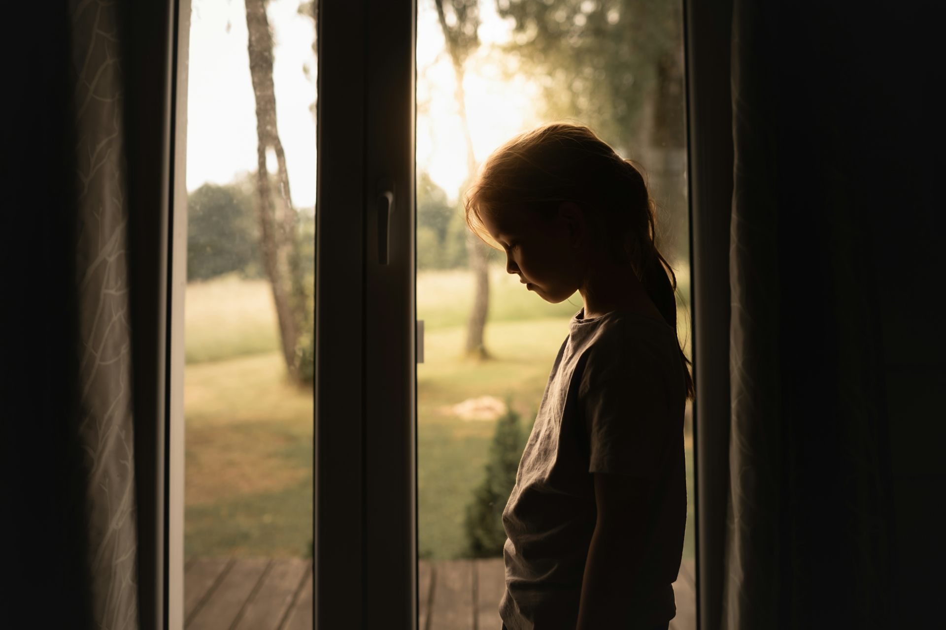 Sad girl standing at a patio door.
