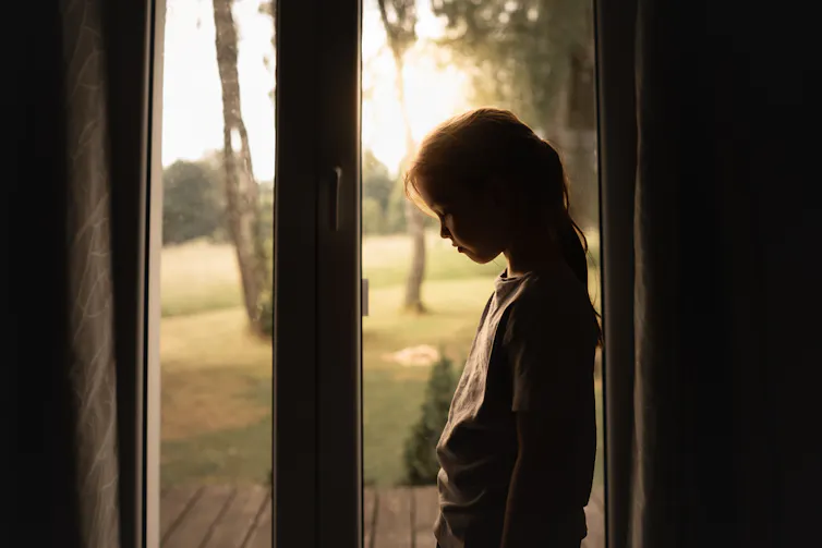 Sad girl standing at a patio door.