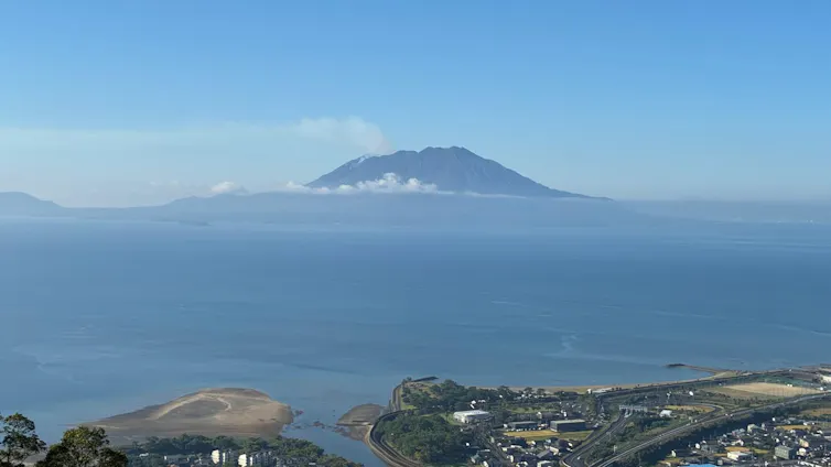 Japanese coastline, volcano in distance, cloud over seascape