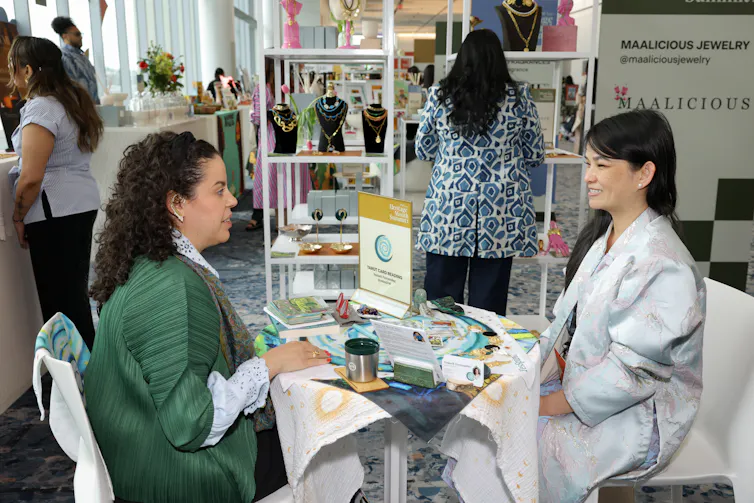 Two women seated at a table with a small display sign reading 'Tarot card reading.'
