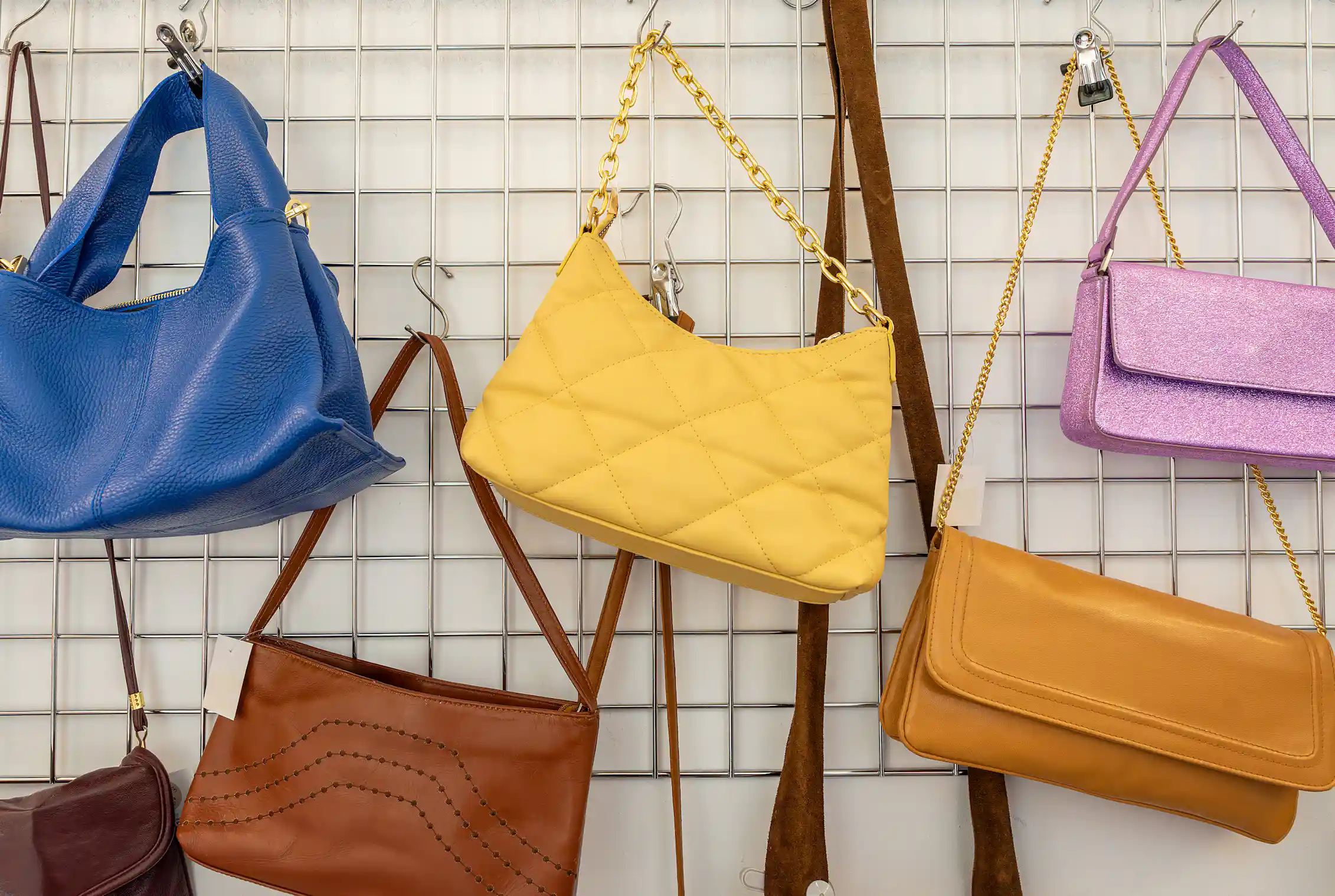 Used purses are hung on a vertical rack along a wall.