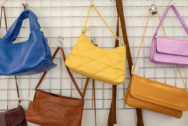 Used purses are hung on a vertical rack along a wall.