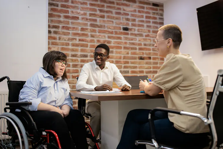 A small group having a conversation in a meeting or shared workspace. One person is in a wheelchair