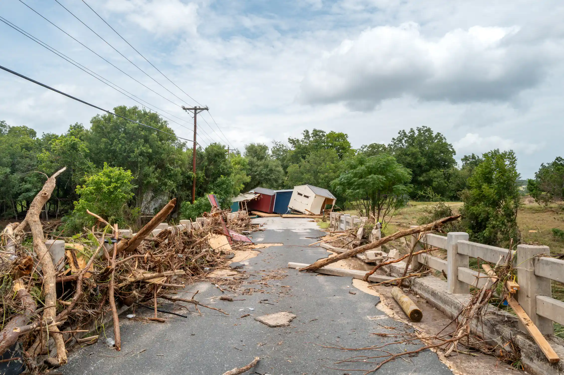 Flood debris has been pushed to the side of a road with two buildings off kilter at the end.