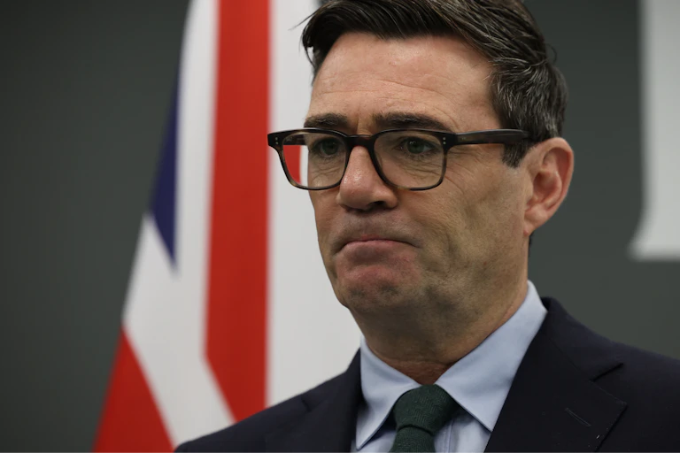 UK Prime Minister Andy Burnham speaks with UK flag in the background.