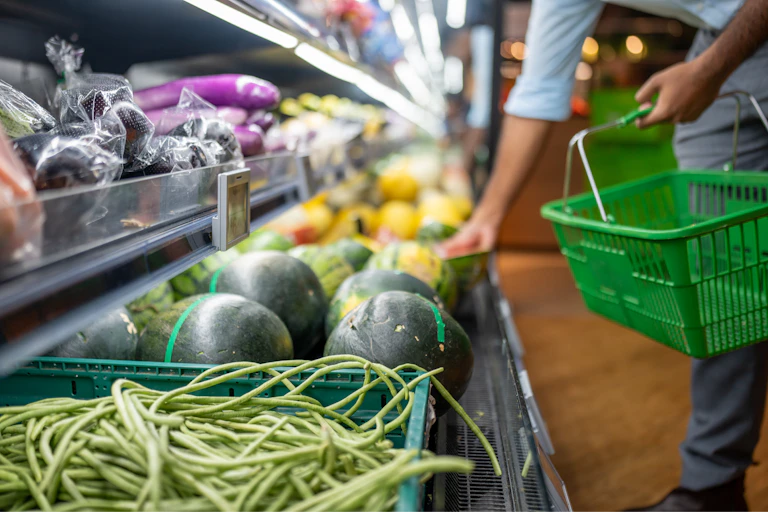 Vegetables in supermarket chiller with person holding shopping basket