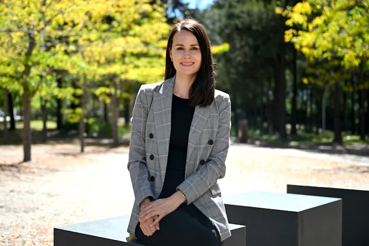 A photograph of Kylie Moore-Gilbert, a smiling woman with dark brown hair, sitting down with trees in the background.