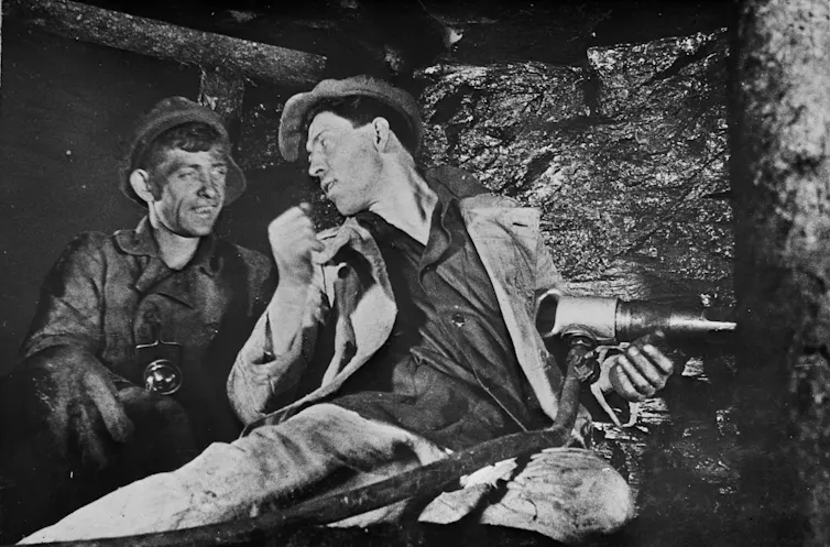 A photograph of two miners talking to each other in a mine.