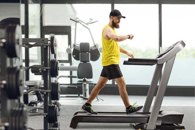 A man walking on a treadmill in the gym checks his smartwatch.