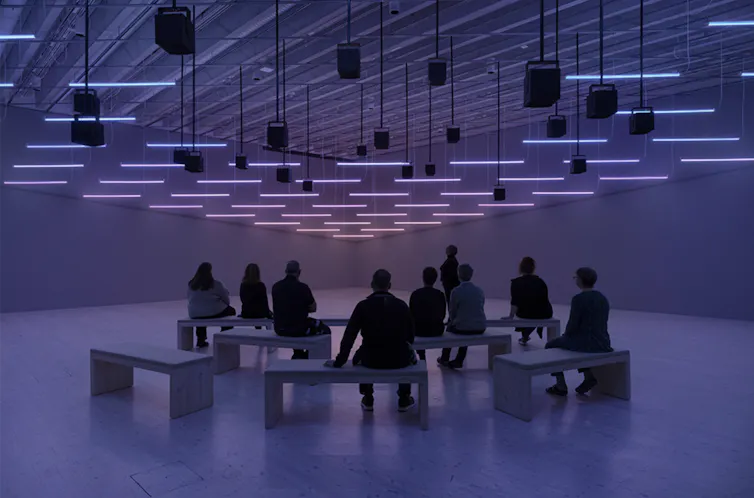 A purple lit interior of an art gallery showing people looking at an installation.