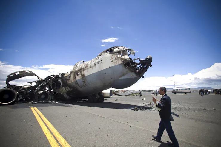 A man walks by the shell of a destroyed airplane fuselage.