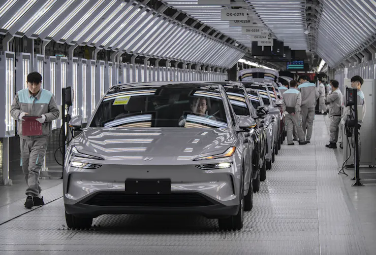 Workers move alongside a row of cars on an assembly line.