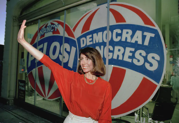 A brown-haired woman standing in front of a campaign sign, waving.