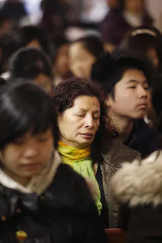 About half a dozen people, some closing their eyes in prayer, sit in church pews.