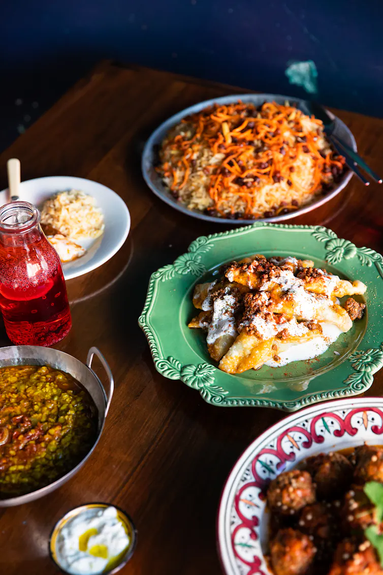 Dishes of food on colourful plates on a wooden table, with a dark blue wall in the background.