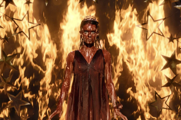 Carrie covered in blood and surrounded by flames in a prom queen tiara.