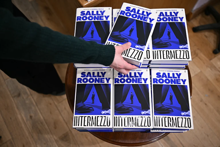 Mano cogiendo un libro de entre las pilas de la novela de Sally Rooney, Intermezzo.