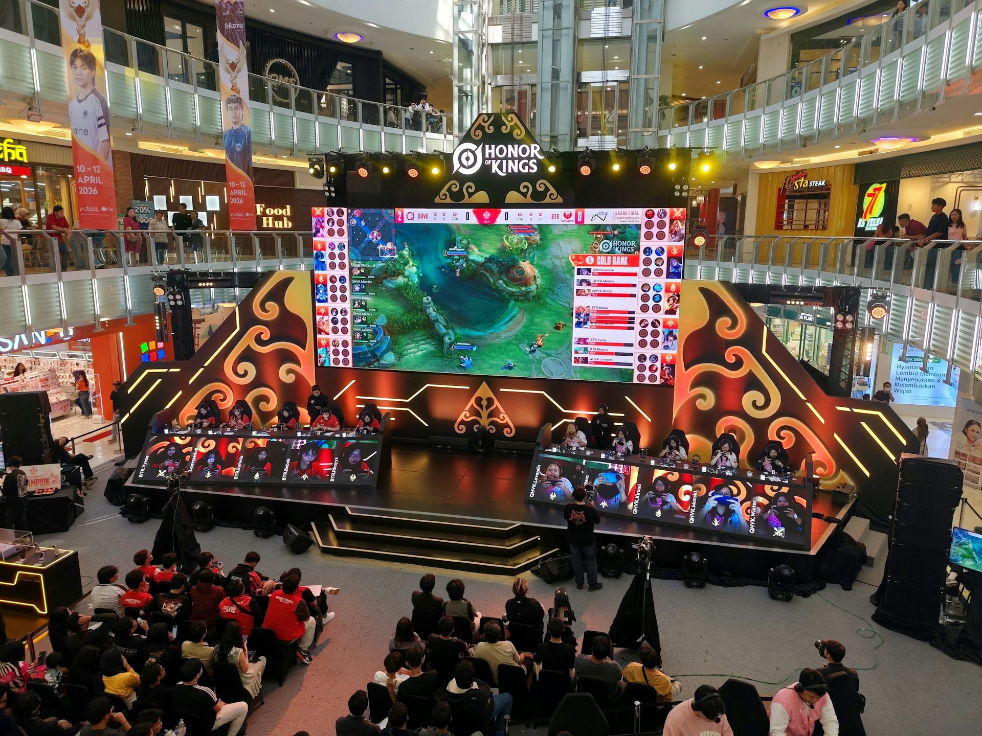 Gamers sat on a stage competing in an Honor of Kings tournament as an audience watches on.