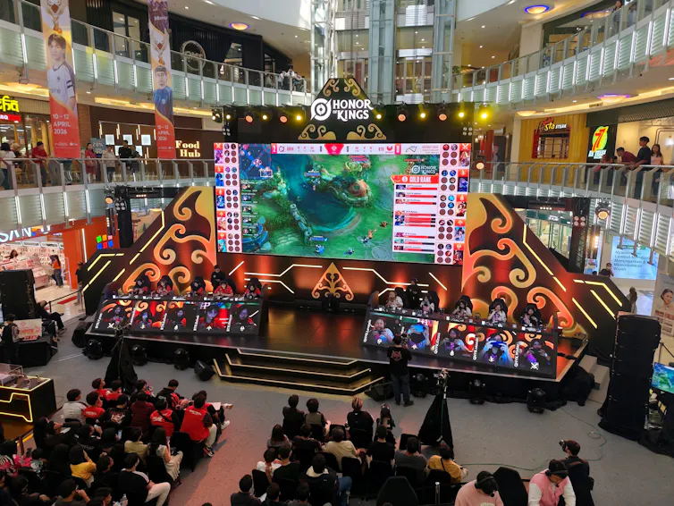 Gamers sat on a stage competing in an Honor of Kings tournament as an audience watches on.