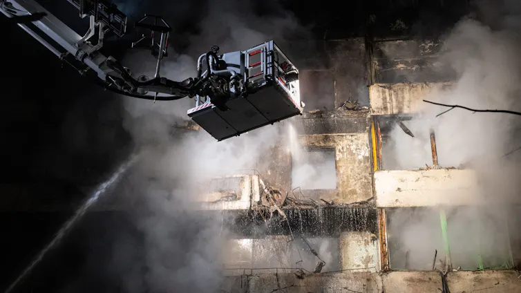 A man on a crane sprays water on a smoking building.