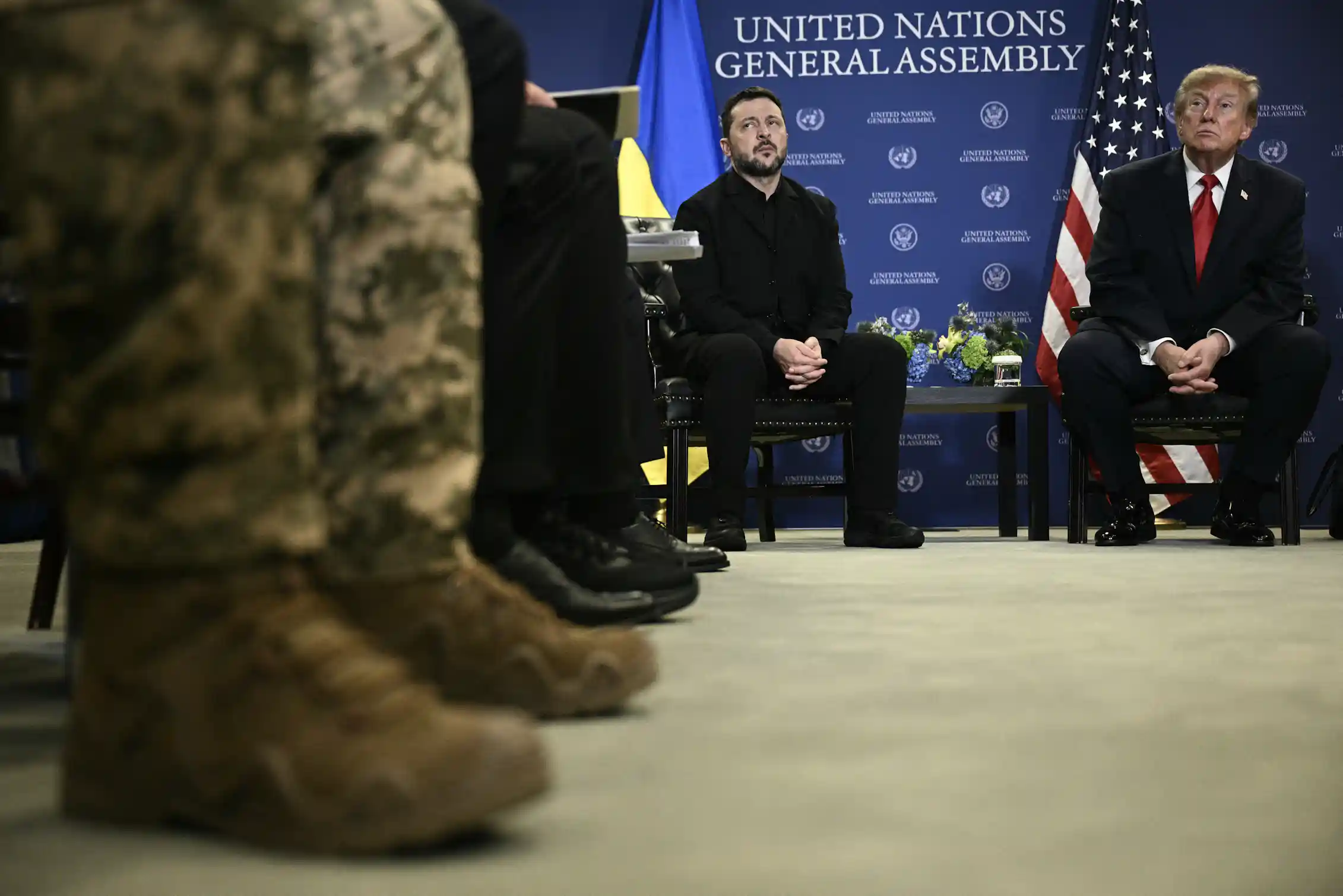 Two men sit in the background with army boots seen in the foreground.