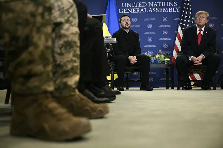 Two men sit in the background with army boots seen in the foreground.